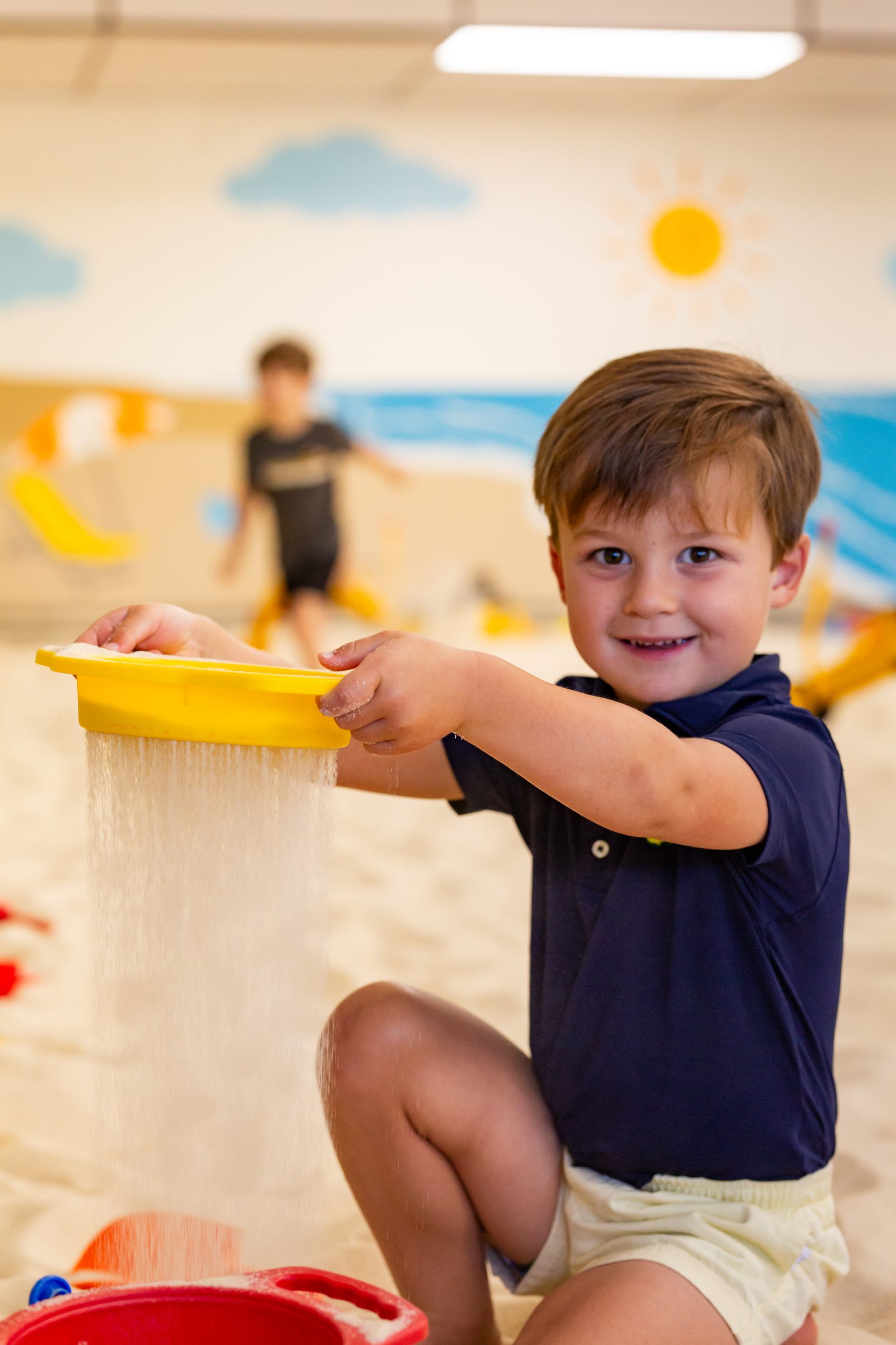 Boy sifting sand through a yellow sieve