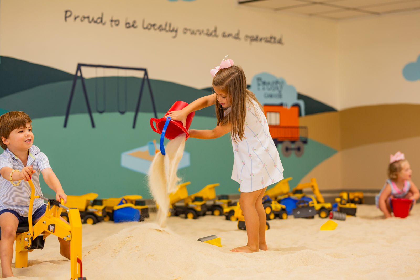 Kids pouring buckets of sand in front of the mural